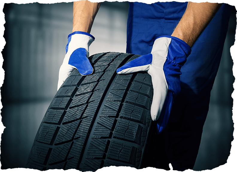 Mechanic holding new tyre on garage background